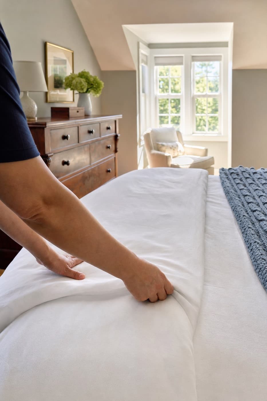 Cleaner smoothing a freshly made bed in a Cape Cod bedroom
